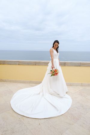 A flowing white wedding dress spread out on a sandy beach with ocean waves in the background.