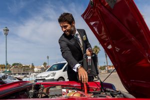 Person examining under the hood of a classic red car on a sunny day.