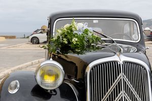 Classic black vintage car decorated with greenery and flowers parked on a street.