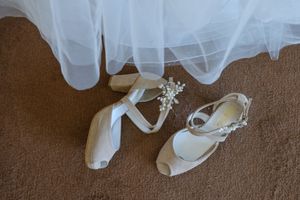 Close-up details of a flowing white wedding dress train on brown carpet.