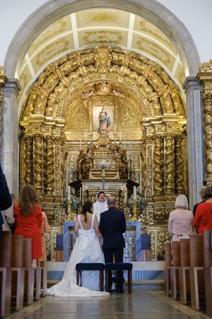Interior of a grand church with golden baroque altar and rows of wooden pews.