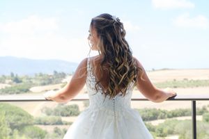 A person in a white wedding dress looks out over a scenic mountain landscape from a balcony.