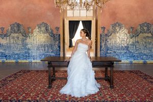 Bride in white gown poses against wall with ornate blue Portuguese azulejo tiles and crystal chandelier.