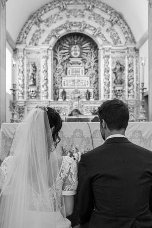 Couple sitting in church pews facing ornate baroque altar during wedding ceremony.