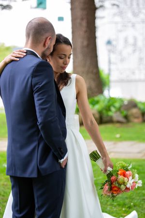 Couple in wedding attire posing together on grassy lawn with floral bouquet.