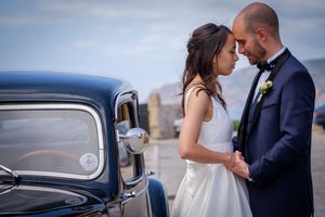 Romantic wedding portraits with a classic car against seaside backdrop.