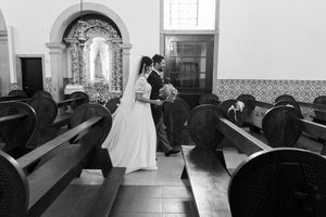 Black and white photo of newlyweds walking down church aisle between wooden pews.