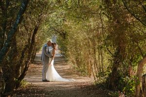 Newlyweds walking through a natural tunnel of trees on a sunlit forest path.