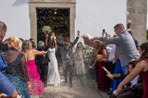 Wedding guests throwing confetti at newlyweds exiting church doorway in celebratory moment.
