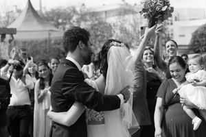 Black and white celebration photo of newlyweds embracing while crowd cheers with joy.