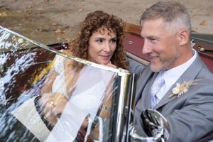 Wedding couple sharing an intimate moment in vintage car with reflective surfaces.
