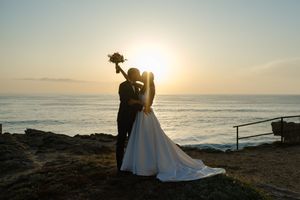 Silhouetted wedding couple against dramatic ocean sunset sky.