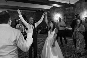 Wedding reception guests dancing and celebrating with raised arms in a dimly lit venue.