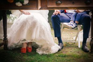 Fun detail shot of bride in red shoes and groom's feet during an outdoor wedding.