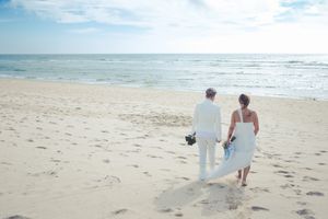 A couple walks hand in hand along a pristine beach with ocean waves in the background.