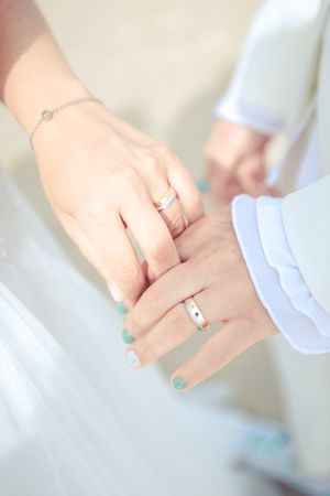 Close-up of wedding rings and intertwined hands with mint green nail polish.