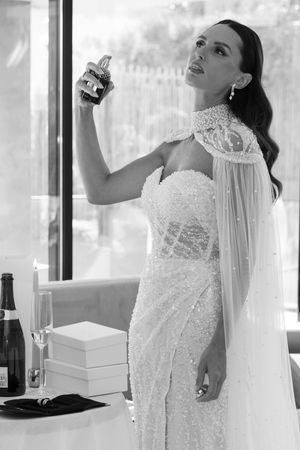 A bride in a beaded lace gown poses by window in black and white photography.