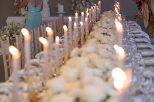 Elegant wedding table setting with white flowers and glowing candles in soft focus.