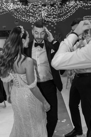 Newlyweds share a joyful dance moment under twinkling lights at their wedding reception.
