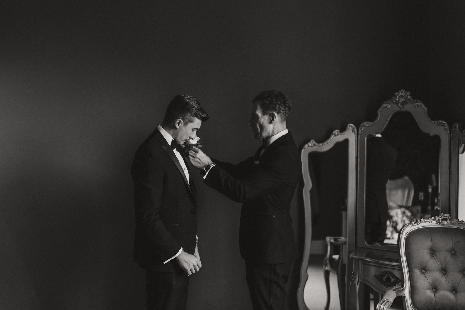 Two people in formal suits helping each other get ready before a wedding event at Hirst Priory.