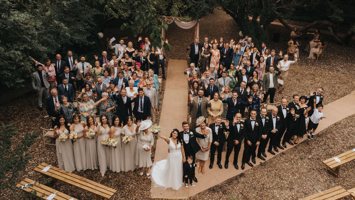 Aerial view of a wedding party standing in formation on a winding dirt path surrounded by trees at Hirst Priory.