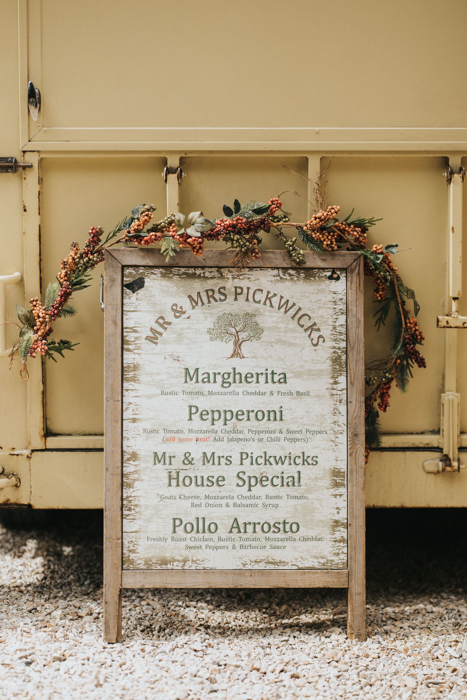 Rustic wooden menu signs with distressed finish display pizza varieties and specials on a beige wall with floral decorations at Hirst Priory