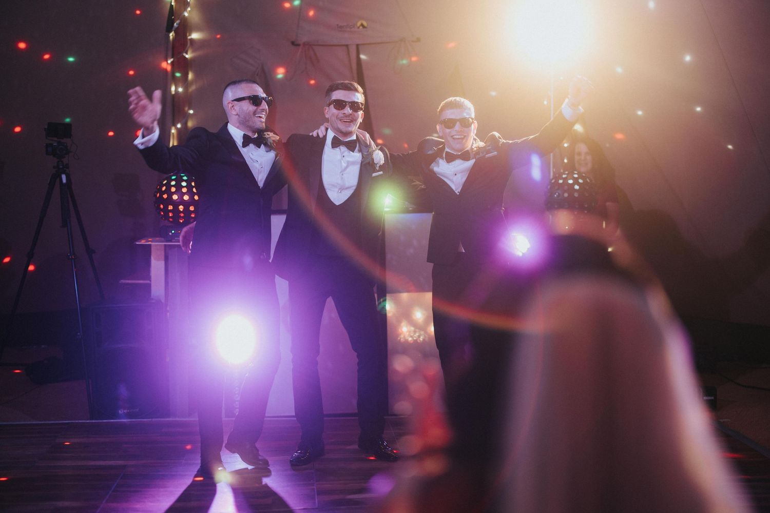 Groomsmen performing on stage with dramatic purple and orange lighting creating an atmospheric concert ambiance at Hirst Priory.