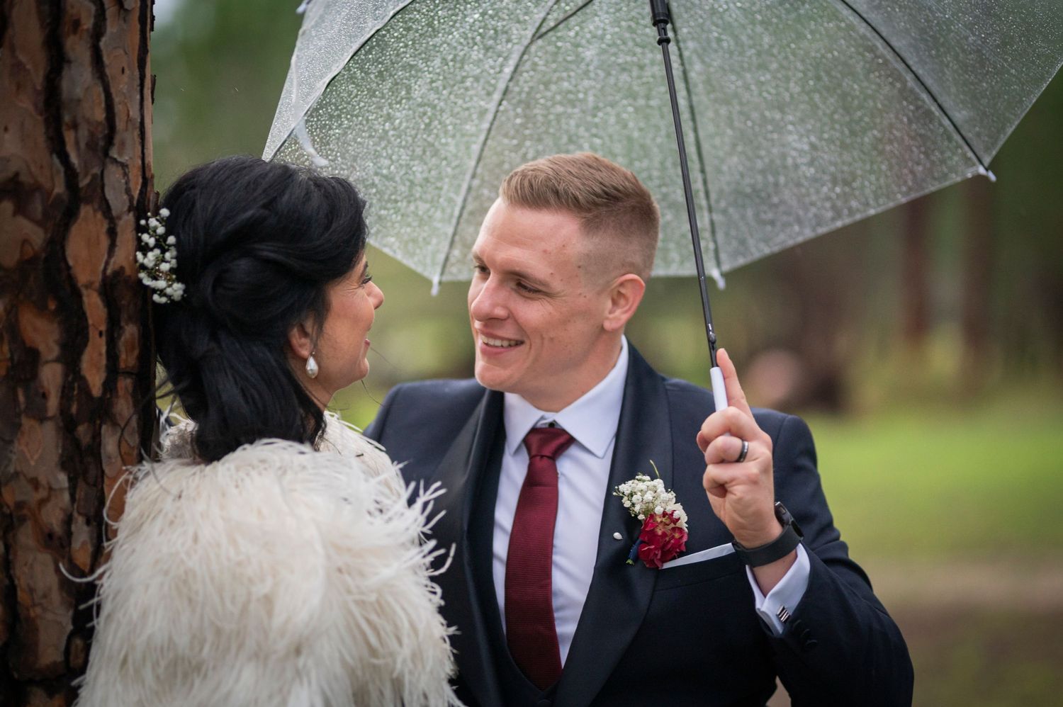 Happy couple shares an intimate moment under silver umbrella at outdoor wedding ceremony on rainy day.