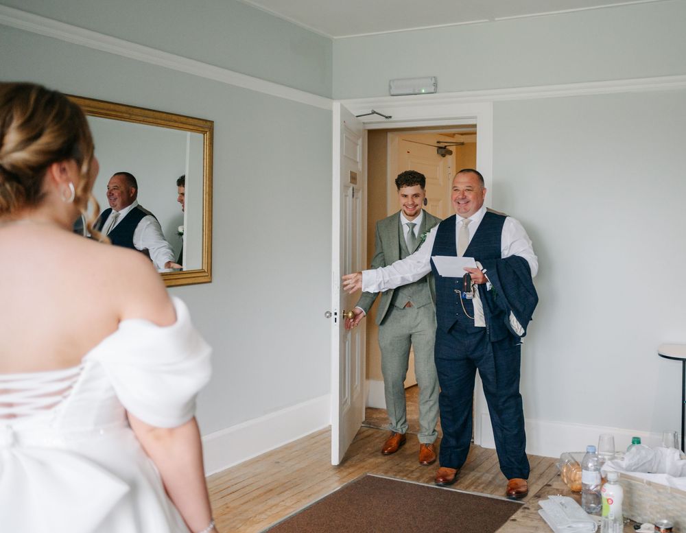 Natural light wedding preparation scene in a bright hotel room with mirror reflection.