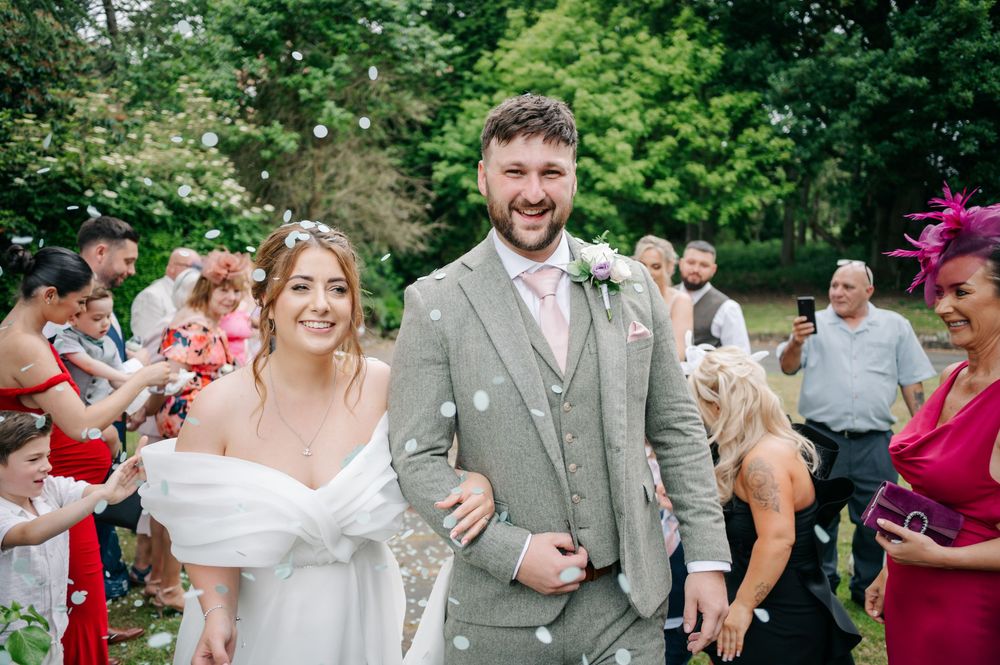 Wedding party celebrates joyfully in a lush garden setting as guests react with laughter and smiles during a candid moment.