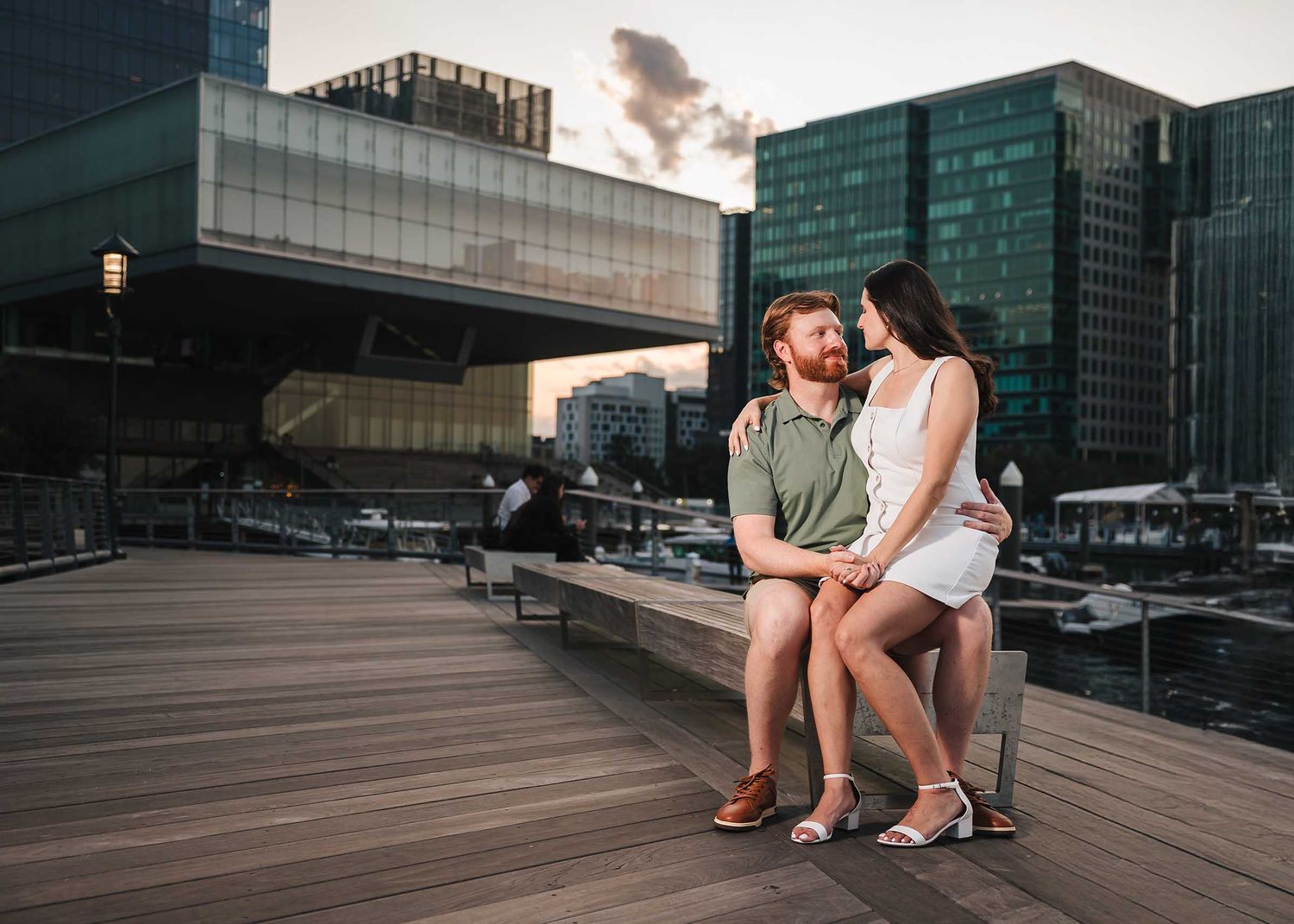 The engaged couple hold hands and look into each other's eyes while sharing a romantic moment in the seaport neighborhood of Boston.