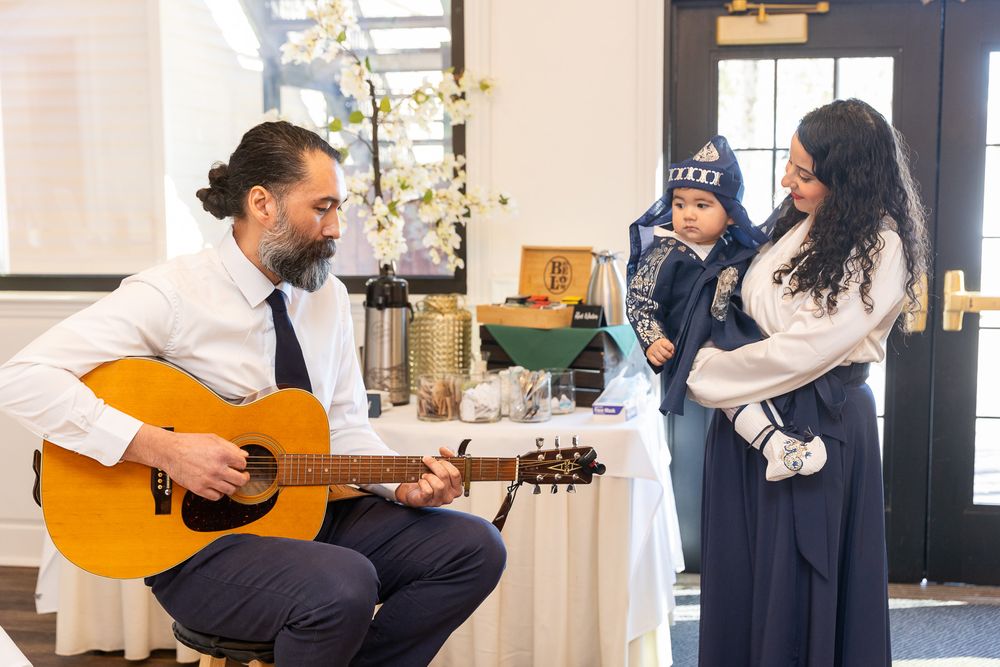 A musician plays acoustic guitar while entertaining a small group in a bright indoor space.