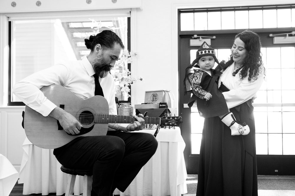 Musicians perform together at an indoor venue with one playing acoustic guitar and another singing in black and white.
