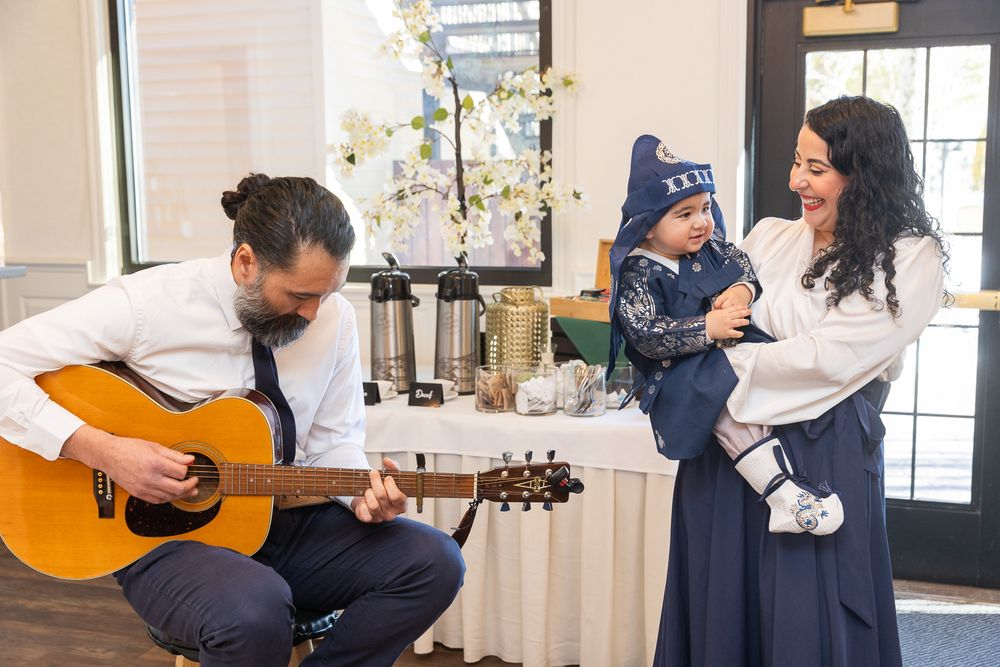 Someone plays acoustic guitar while others enjoy a musical moment in a brightly lit living room decorated with white flowers.