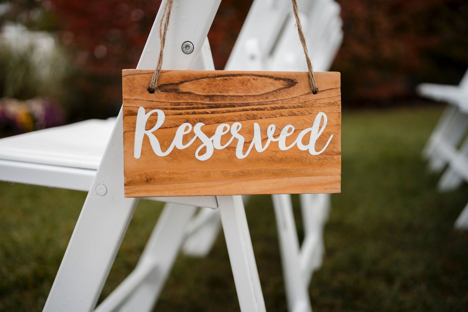 Wooden 'Reserved' sign on white folding chair at outdoor wedding venue.