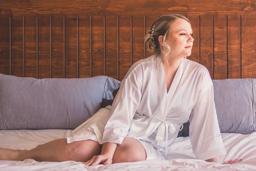 Person in white bathrobe relaxes on bed with striped pillows against wooden headboard.