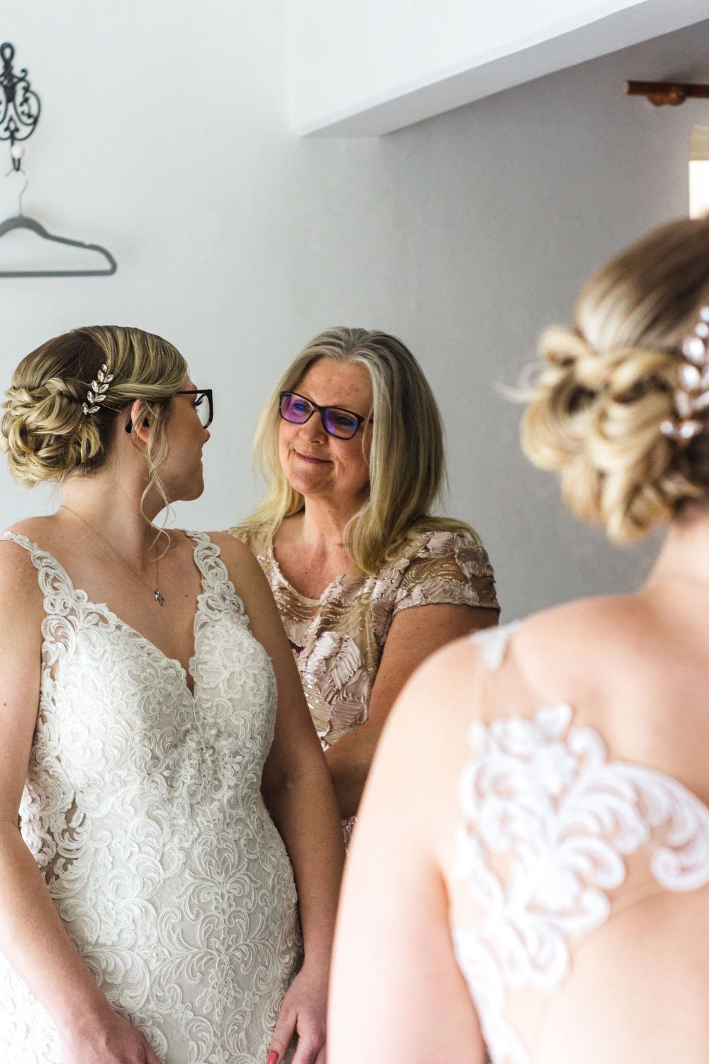 Elegant lace wedding dress details shown with three people in a room with soft natural lighting.