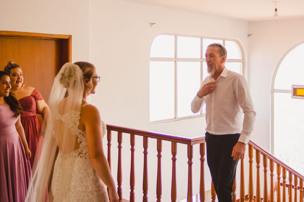 In a sunlit stairwell, a bride in a flowing white gown and veil shares a tender moment with loved ones.