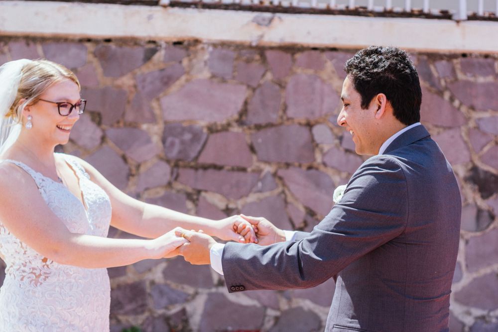 A couple shares a tender moment exchanging rings during an outdoor ceremony against a rustic stone wall.