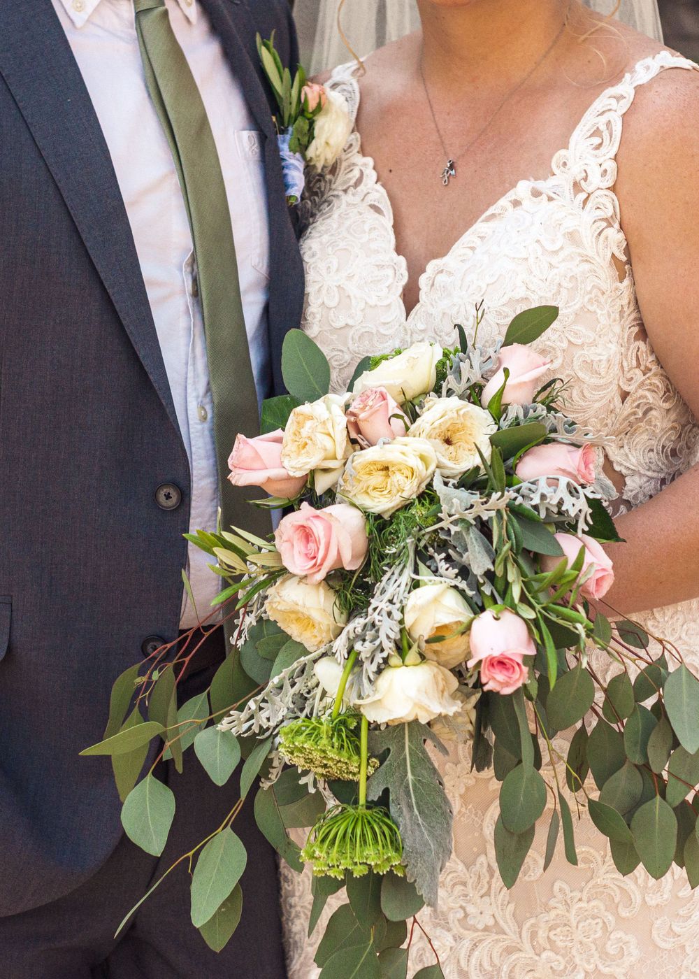 Beautiful wedding bouquet with pink and cream roses, eucalyptus leaves against white lace dress and navy suit.