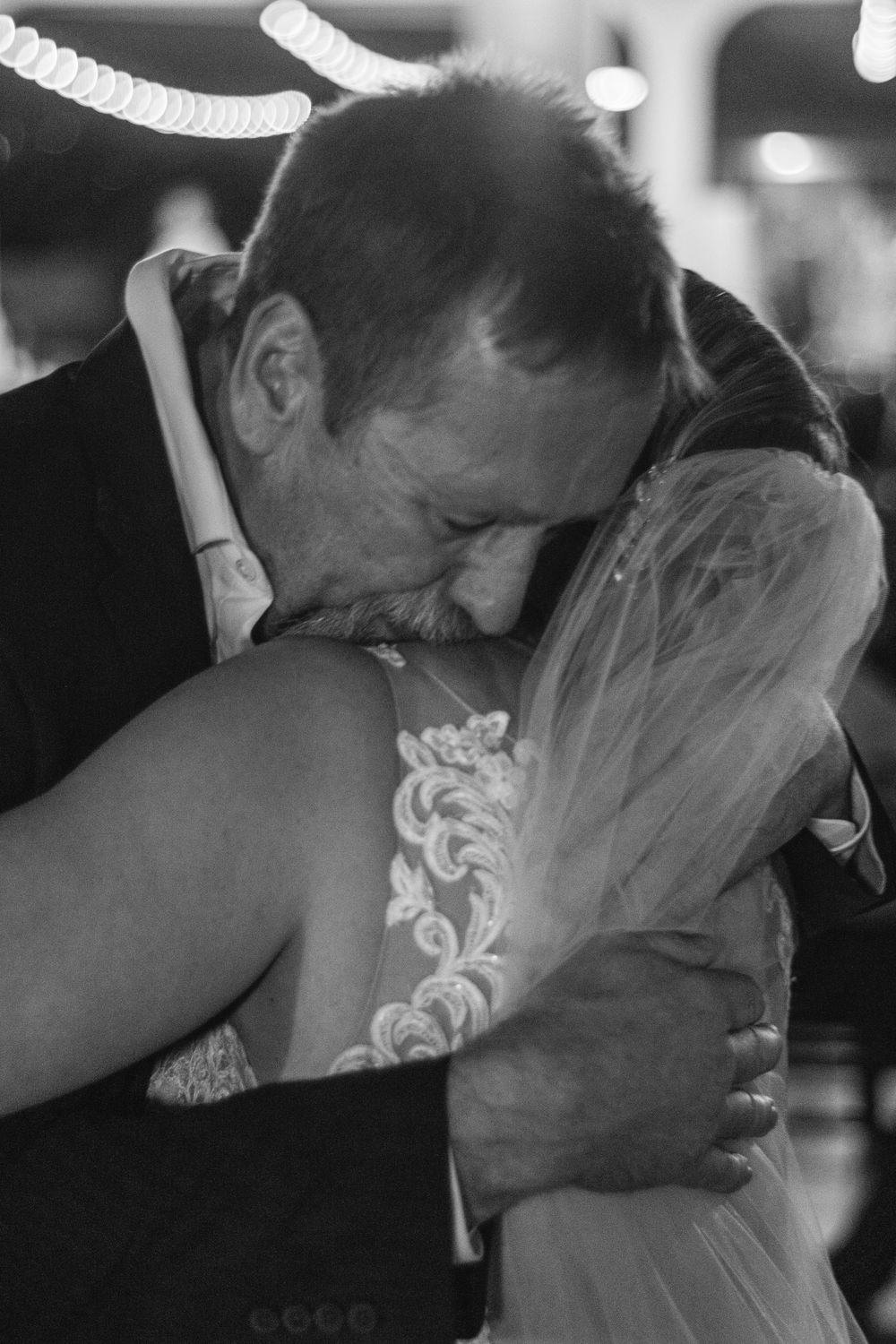 A tender black and white moment between a couple embracing in formal wedding attire with delicate lace details.