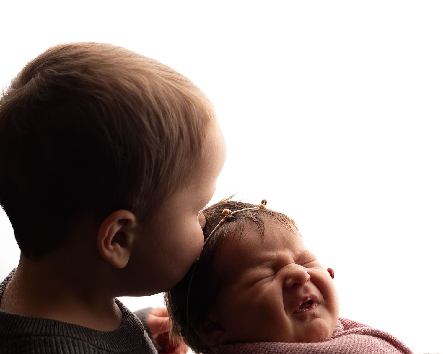 Professional photo of a newborn baby being kissed by her big brother