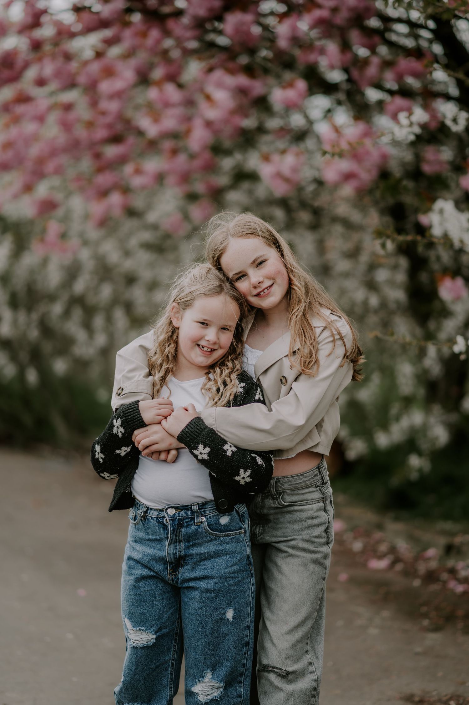 Two young people in casual denim outfits embracing under blooming pink cherry blossoms on a spring day.