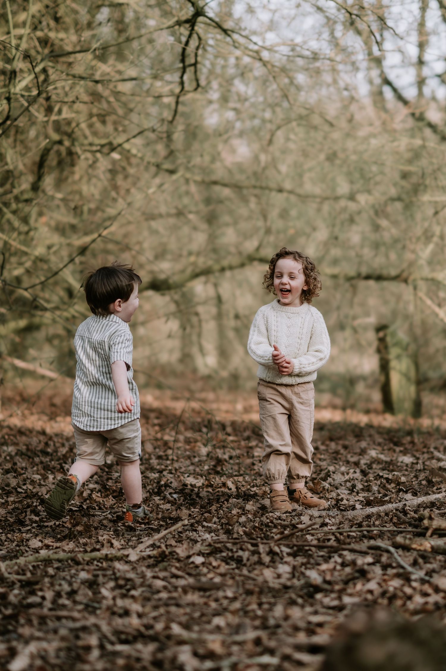 Two children play and laugh together on a leaf-covered forest floor during autumn.