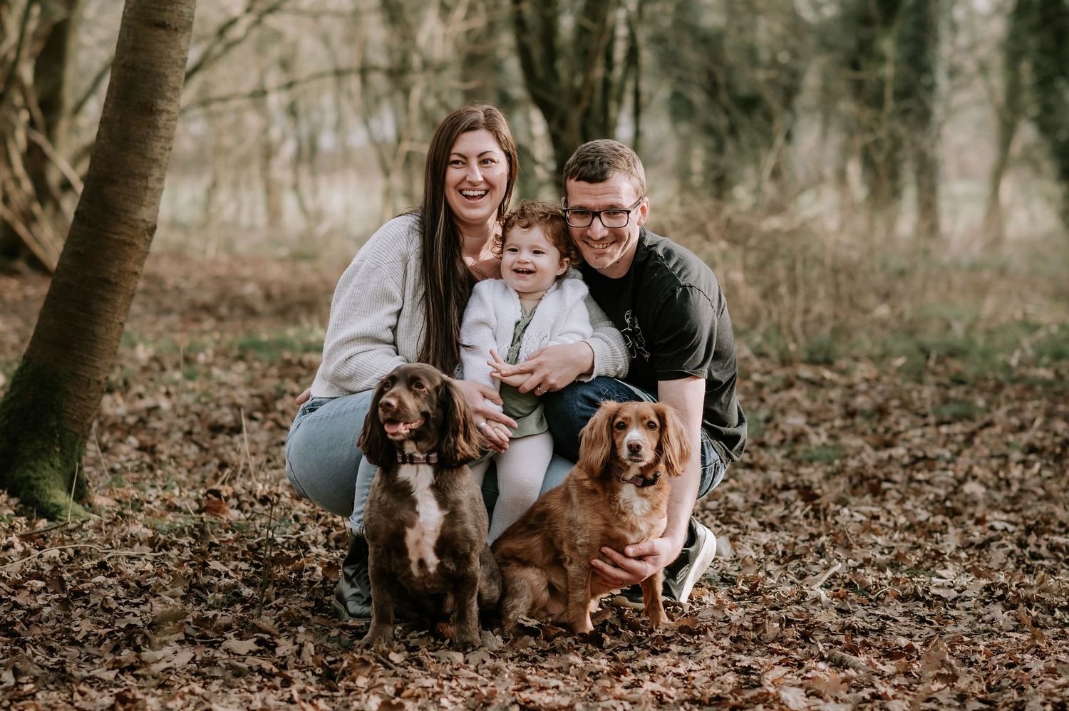 A group poses with two friendly dogs in a serene forest setting during autumn.