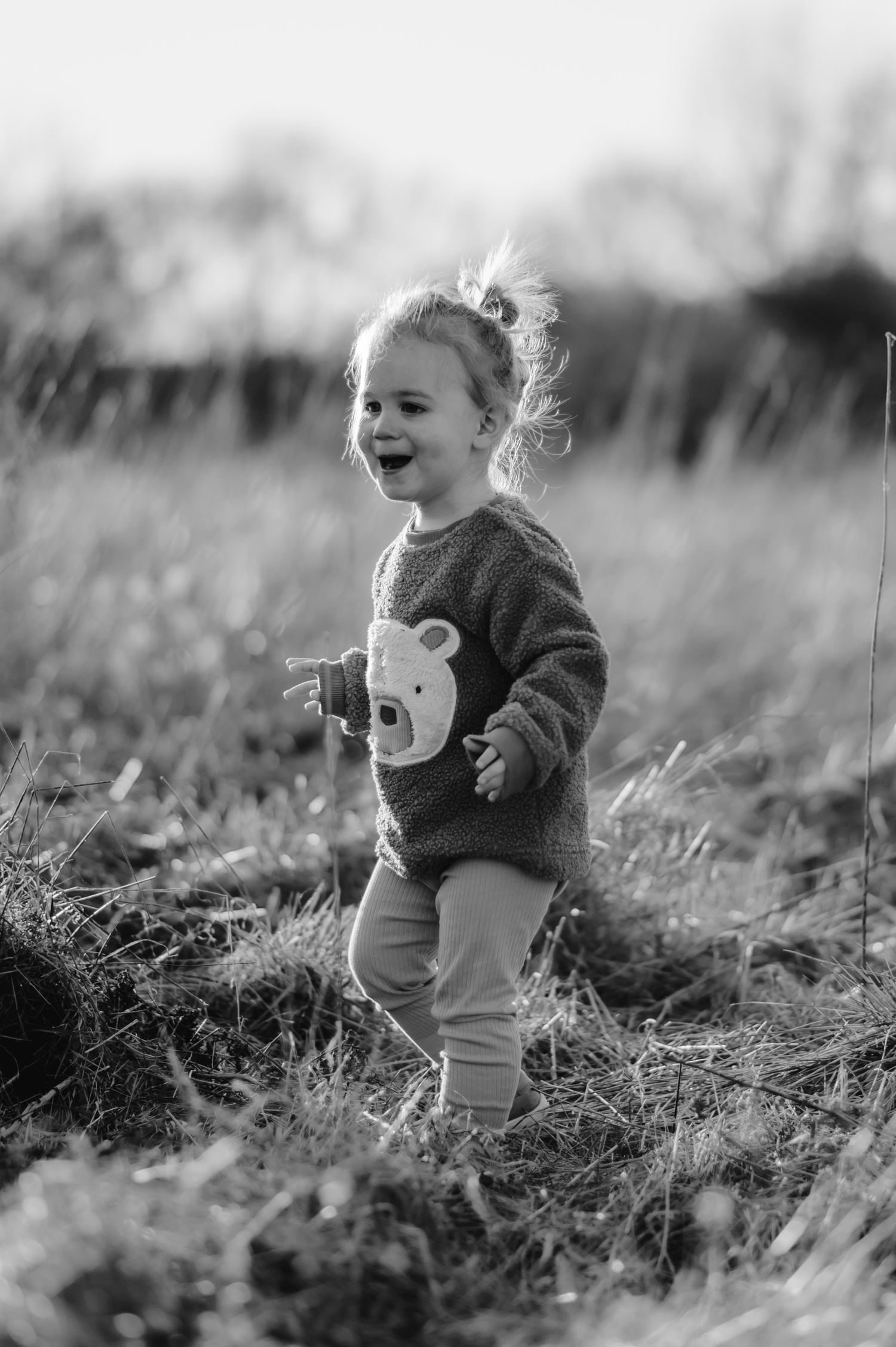A joyful child wearing a sweater with an animal design runs through a tall grass field in black and white.