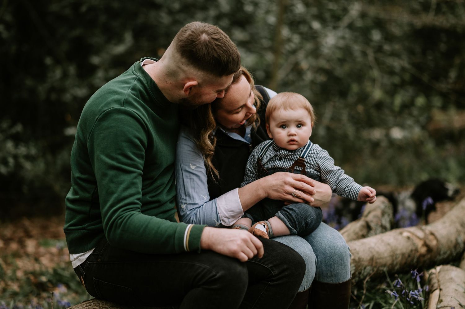 A family enjoying a tender moment together while sitting on a fallen log in an autumn forest setting.