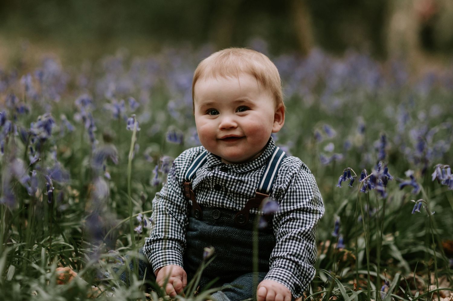 A small child in striped shirt and overalls sits in a field of blooming purple wild flowers on a sunny day.