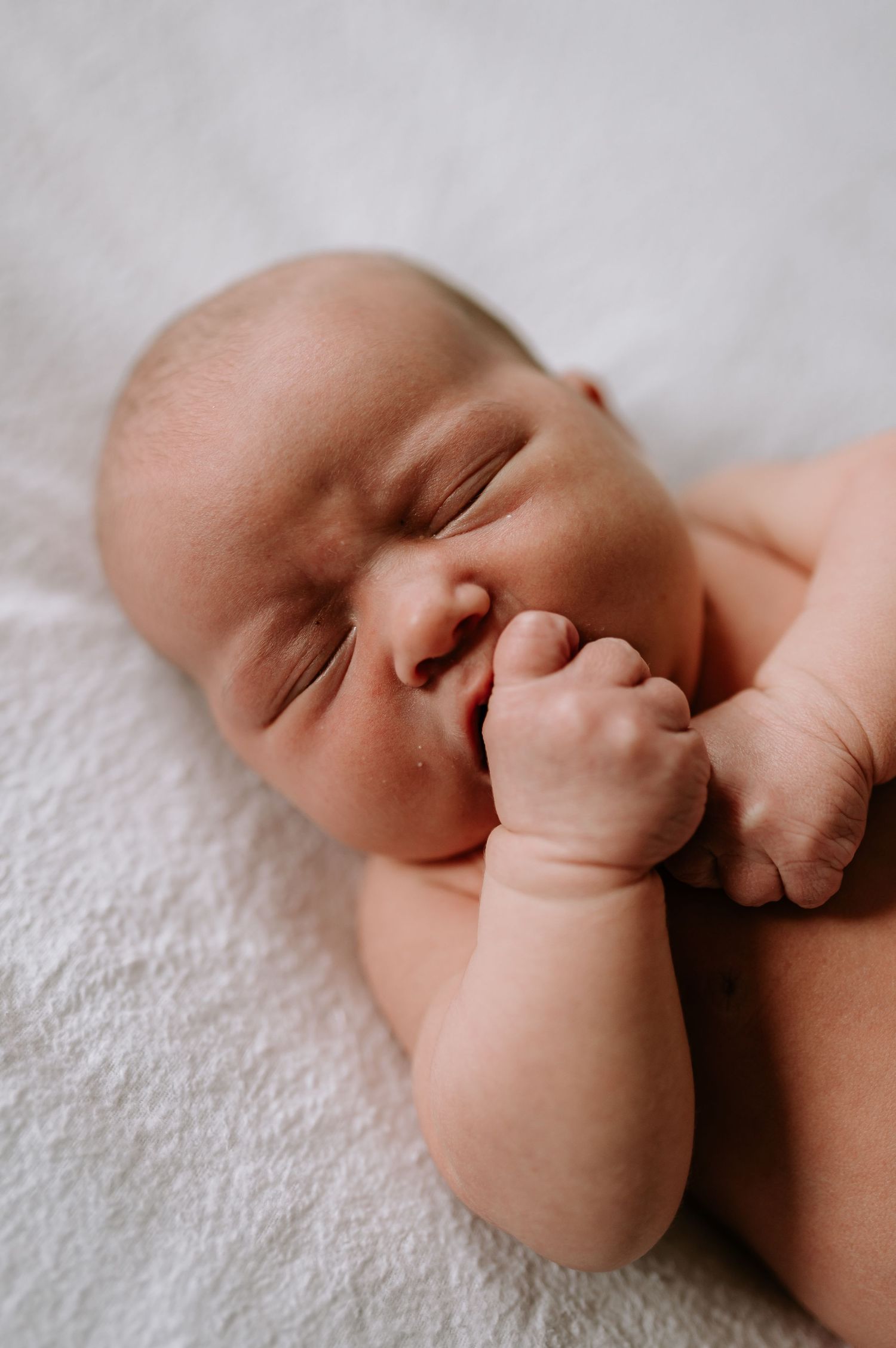 Peaceful sleeping newborn baby rests on soft white blanket with tiny hand near face.