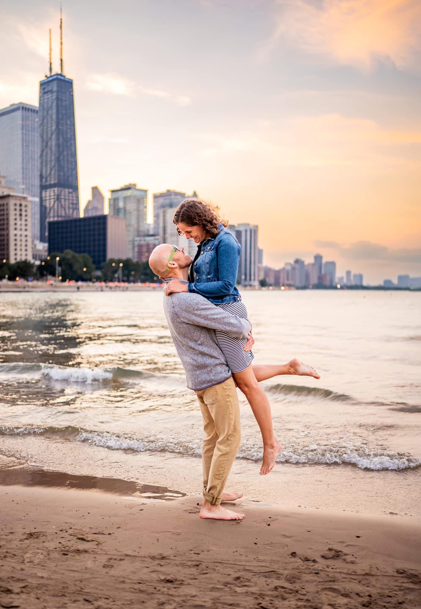 A romantic embrace on North Avenue Beach in Chicago with the iconic John Hancock building and skyline at sunset.